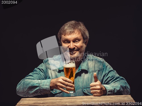Image of The smiling man in denim shirt with glass of beer