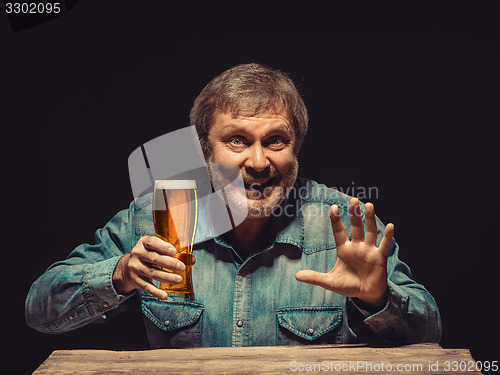 Image of The smiling man in denim shirt with glass of beer