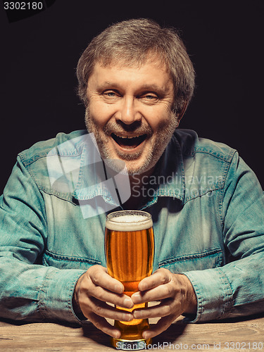 Image of The smiling man in denim shirt with glass of beer