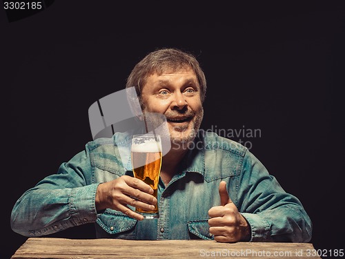 Image of The smiling man in denim shirt with glass of beer