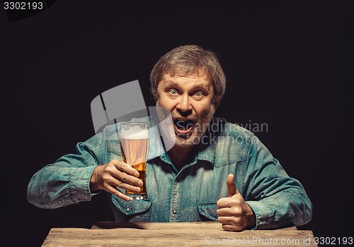 Image of The smiling man in denim shirt with glass of beer