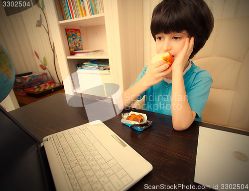 Image of pensive boy sitting with a laptop and eating apple