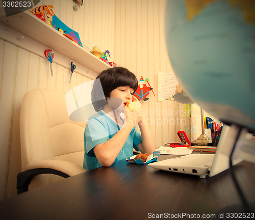 Image of schoolboy with a laptop eating apple