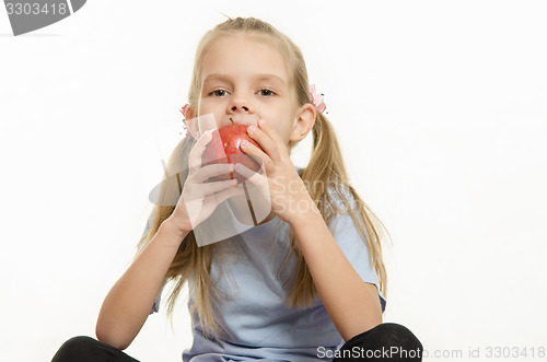 Image of Six year old girl sitting and eating an apple