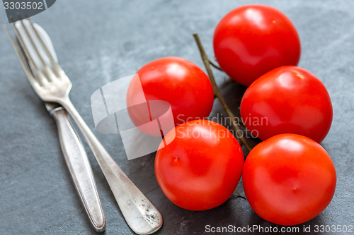 Image of Red tomatoes on a branch, fork and knife.