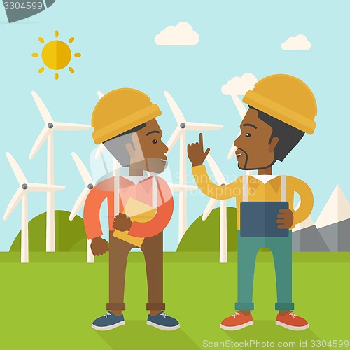 Image of Two black workers talking infront of windmills.