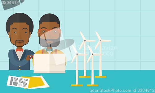 Image of Two black Workers using laptop with windmills.