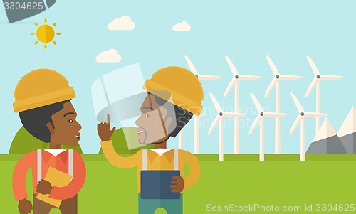 Image of Two black workers talking infront of windmills.