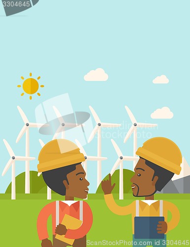 Image of Two black workers talking infront of windmills.