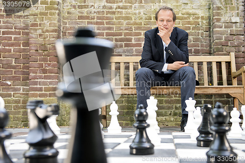 Image of Thinking man sitting at a life sized outdoor chess board