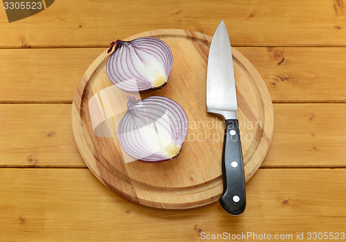 Image of Red onion cut in half with a knife on a cutting board
