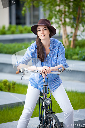 Image of Pretty girl in hat riding a bicycle at street