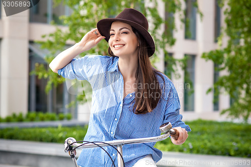 Image of Pretty girl in hat riding a bicycle at street