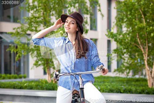 Image of Pretty girl in hat riding a bicycle at street