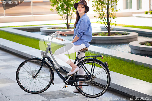 Image of Pretty girl in hat riding a bicycle at street
