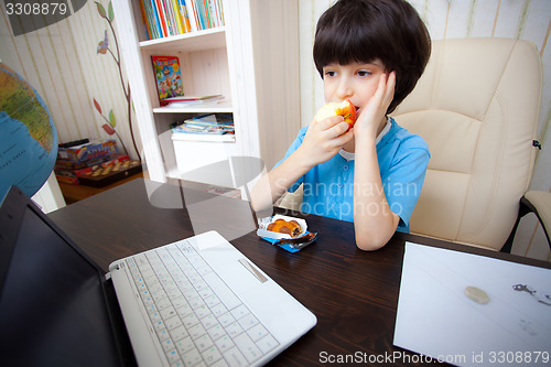 Image of pensive boy sitting with a laptop and eating apple