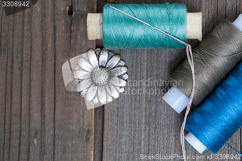 Image of vintage button flower, spool of thread and a sewing needle