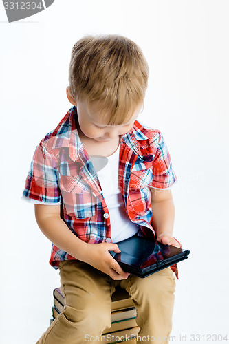 Image of boy sitting on a pile of books with tablet computer