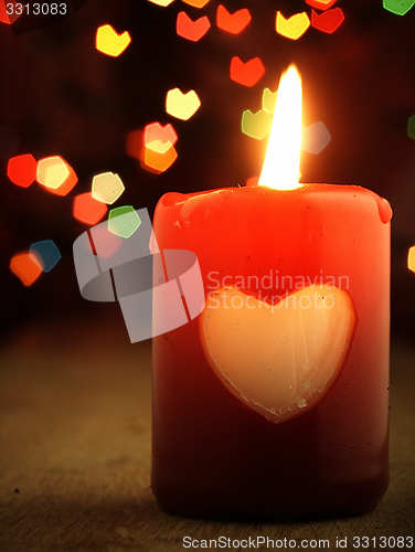 Image of Red candle on the table and shiny hearts in background.