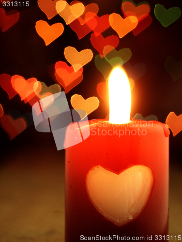 Image of Red candle on the table and shiny hearts in background.