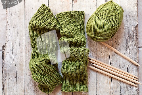 Image of wool green legwarmers, knitting needles and yarn