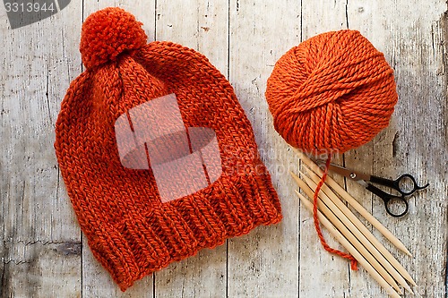 Image of wool orange hat, knitting needles and yarn