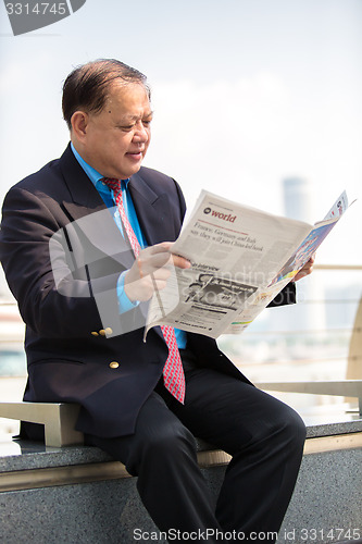 Image of Senior businessman in suit reading newspaper