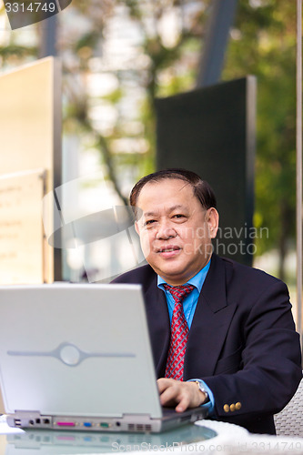 Image of Senior Asian businessman in suit using laptop PC