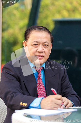 Image of Senior Asian businessman in suit writing business proposal