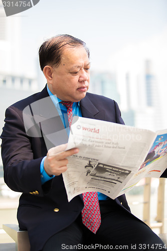 Image of Senior businessman in suit reading newspaper