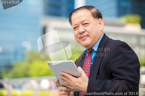 Image of Senior Asian businessman in suit using tablet PC