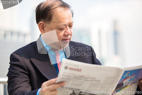 Image of Senior businessman in suit reading newspaper