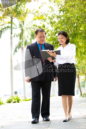 Image of Young Asian female executive and senior businessman walking together