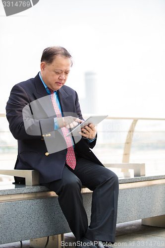 Image of Senior Asian businessman in suit using tablet PC