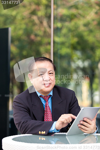 Image of Senior Asian businessman in suit using tablet PC