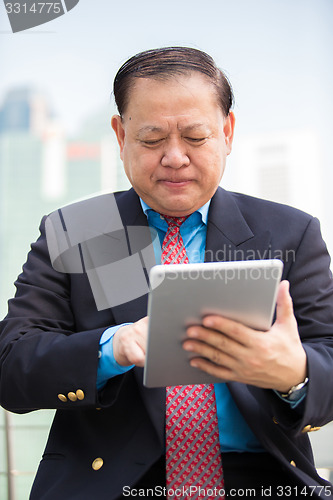 Image of Senior Asian businessman in suit using tablet PC