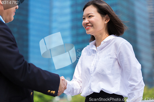 Image of Young Asian female executive and senior businessman shake hands