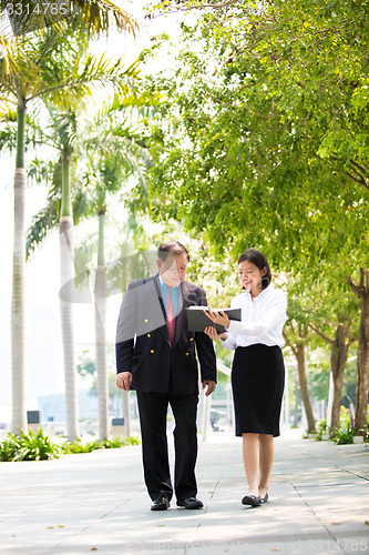 Image of Young Asian female executive and senior businessman walking together