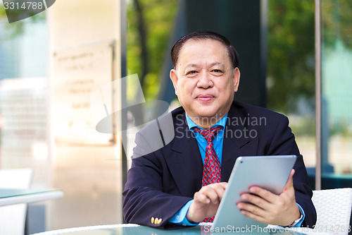Image of Senior Asian businessman in suit using tablet PC
