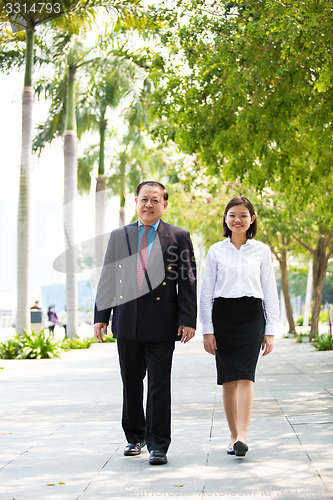 Image of Young Asian female executive and senior businessman walking together