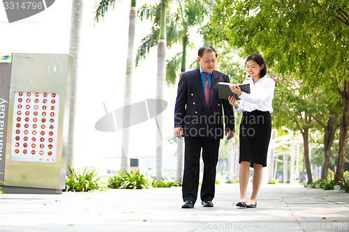 Image of Young Asian female executive and senior businessman walking together