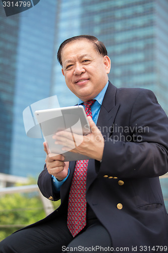 Image of Senior Asian businessman in suit using tablet PC