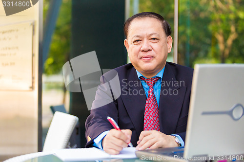 Image of Senior Asian businessman in suit writing proposal