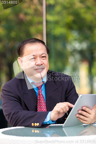 Image of Senior Asian businessman in suit using tablet PC