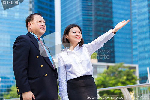 Image of Senior businessman and young female executive pointing at a direction