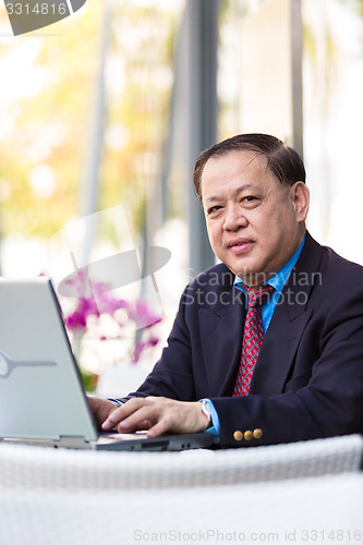 Image of Senior Asian businessman in suit using laptop PC