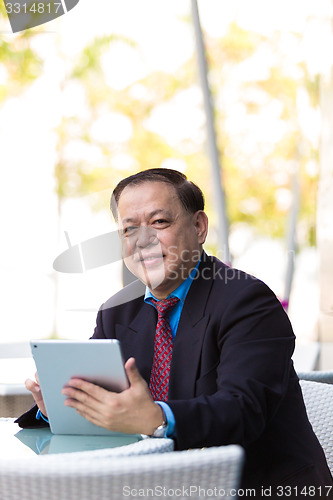 Image of Senior Asian businessman in suit using tablet PC