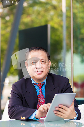 Image of Senior Asian businessman in suit using tablet PC