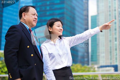 Image of Senior businessman and young female executive pointing at a direction