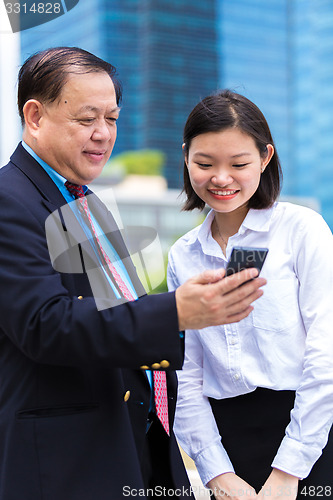Image of Young Asian female executive and senior businessman using smart phone